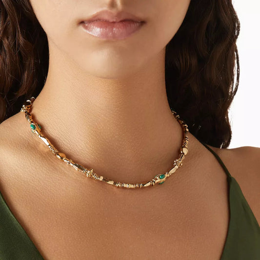 Close-up of a woman wearing a gold necklace with green stones on a white background