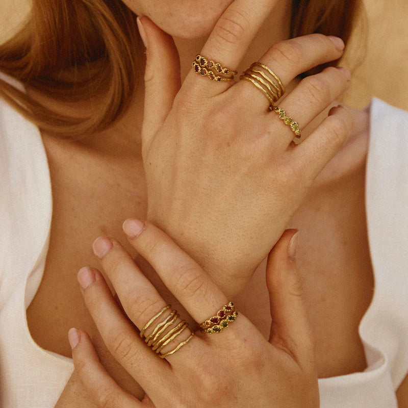 Close-up of hands wearing gold rings with gemstones on a neutral background