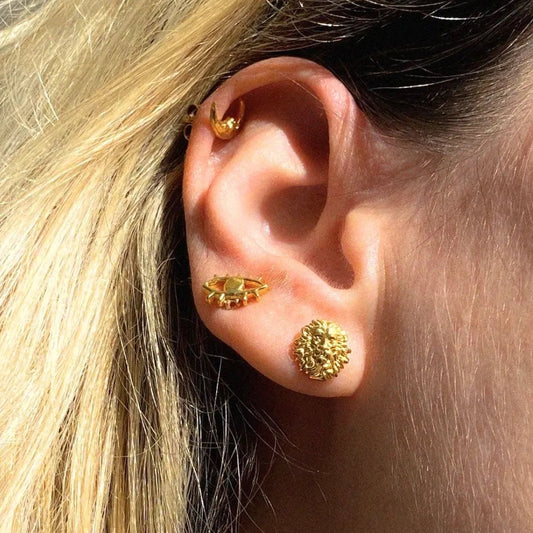 Close-up of an ear wearing gold earrings with blonde hair.