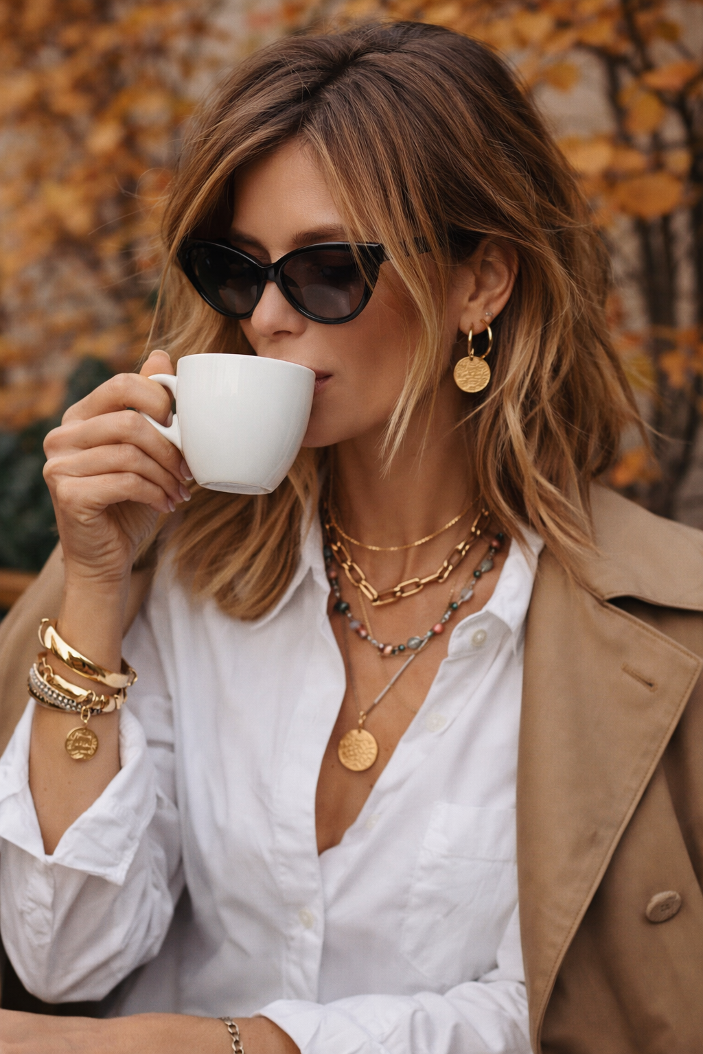 woman wearing white shirt and drinking coffee wearing sunglasses and wearing gold jewellery