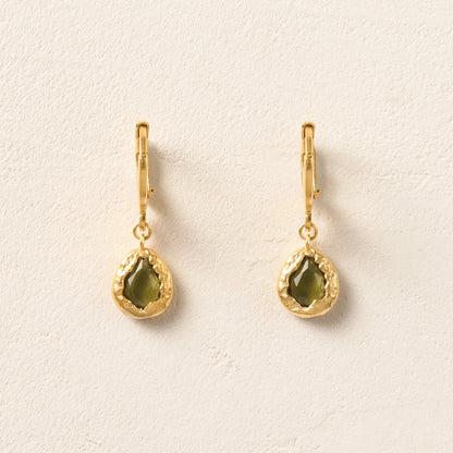 Gold earrings with green gemstones on a light beige background