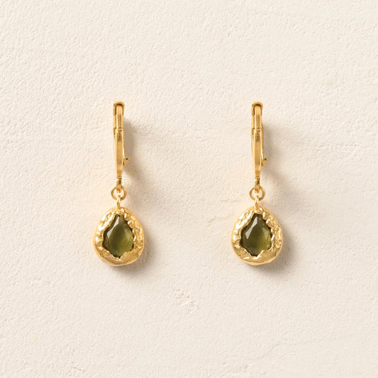 Gold earrings with green gemstones on a light beige background