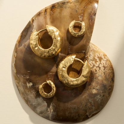 Gold hoop earrings on a textured stone surface