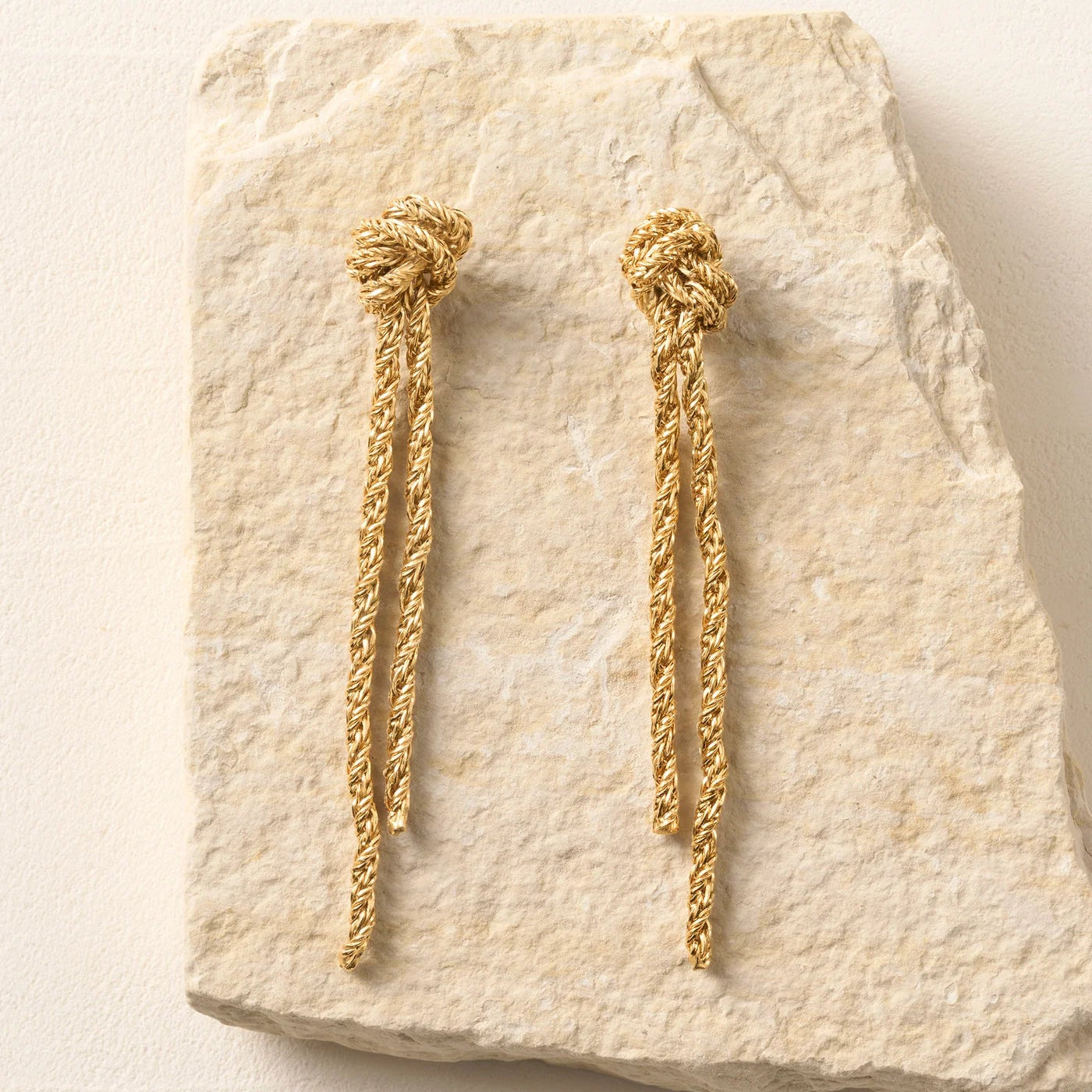 Gold braided earrings on a textured stone surface