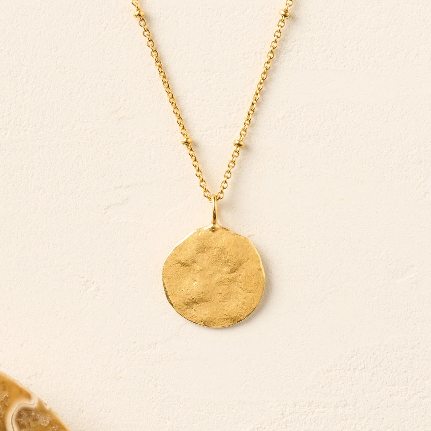 Gold necklace with a round pendant on a beige background