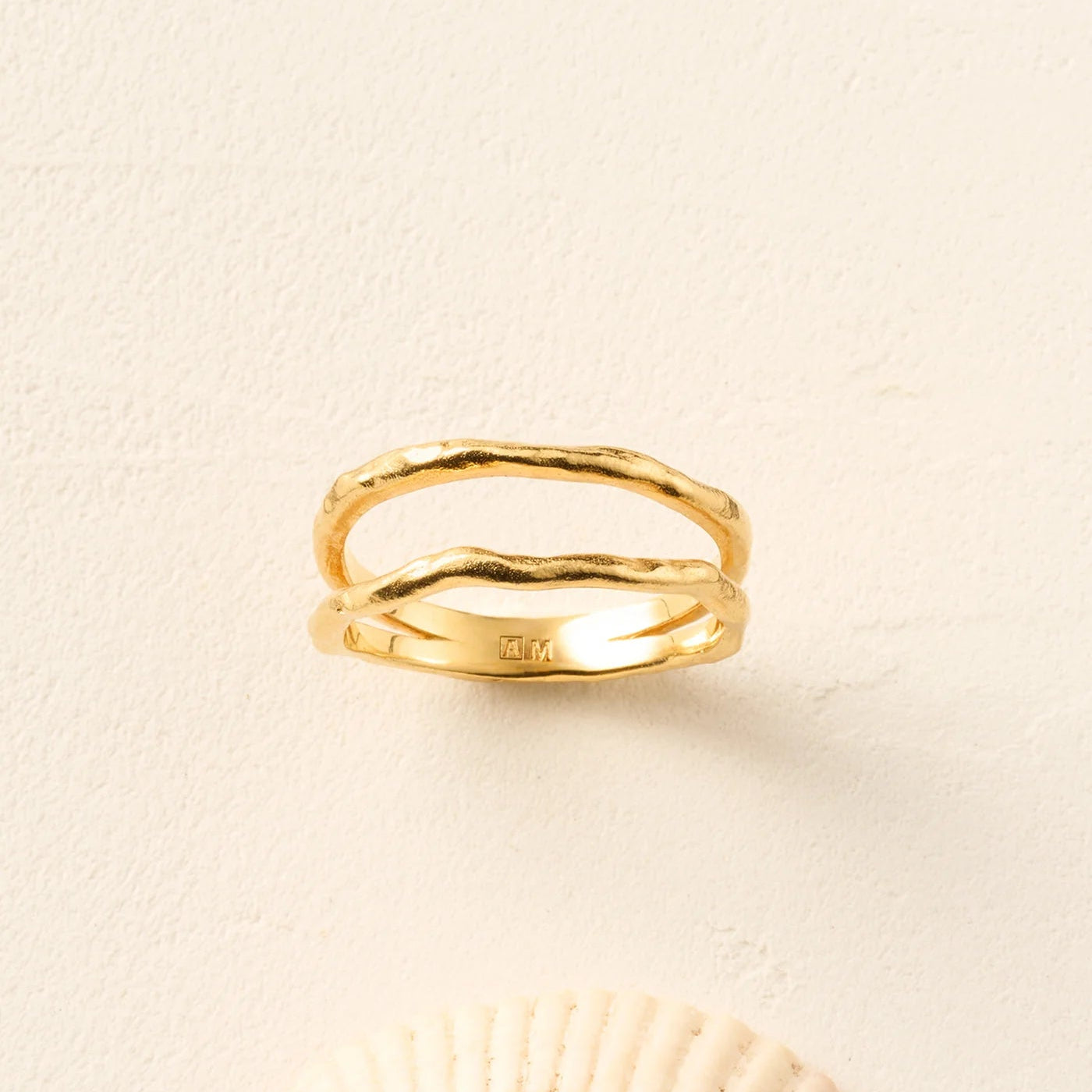 Gold ring on a beige background with a shell at the bottom