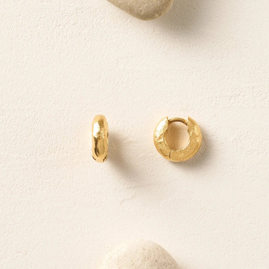 Gold hoop earrings on a light beige surface with stones.