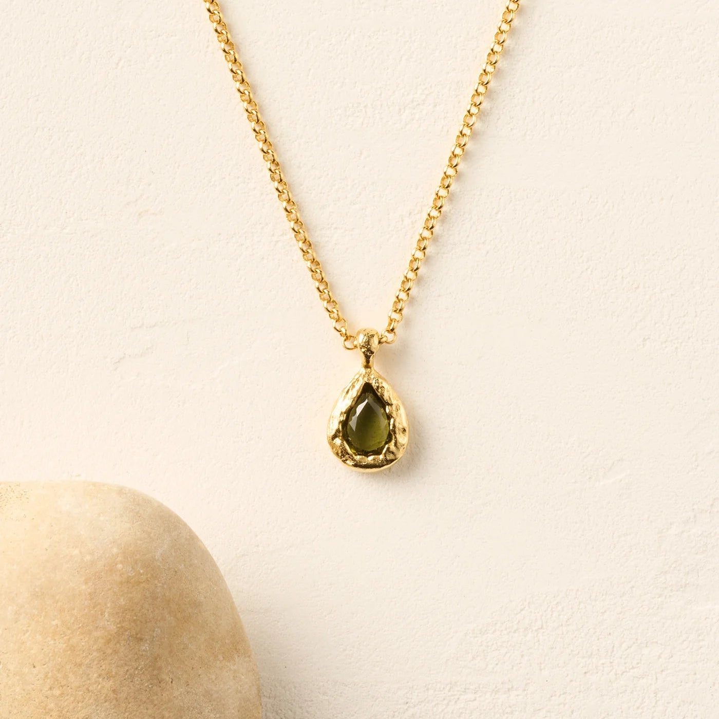 Gold necklace with a green teardrop pendant on a beige background