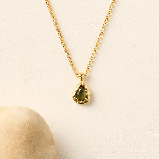 Gold necklace with a green teardrop pendant on a beige background