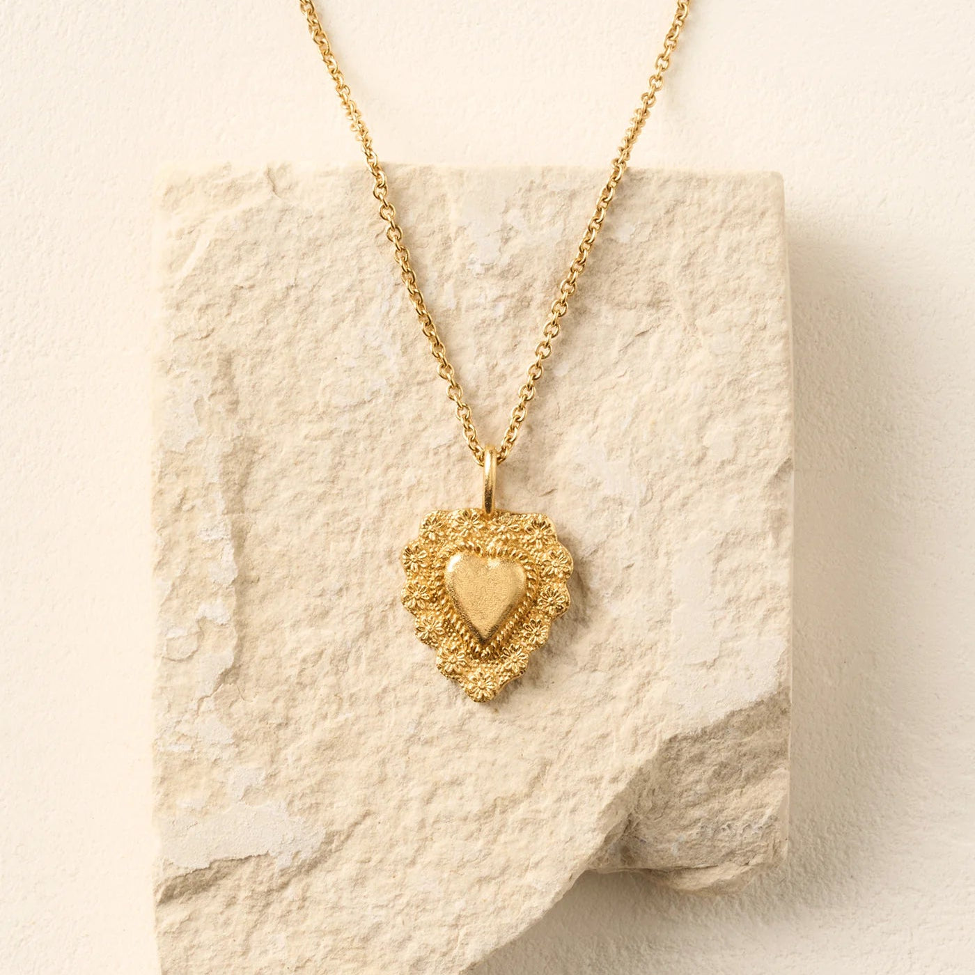 Gold heart-shaped pendant necklace on a textured beige surface