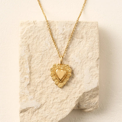 Gold heart-shaped pendant necklace on a textured beige surface