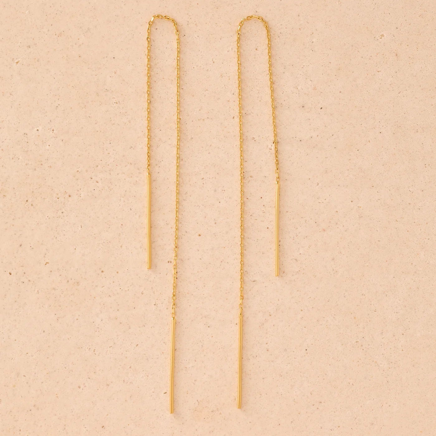 Gold chain earrings on a beige background