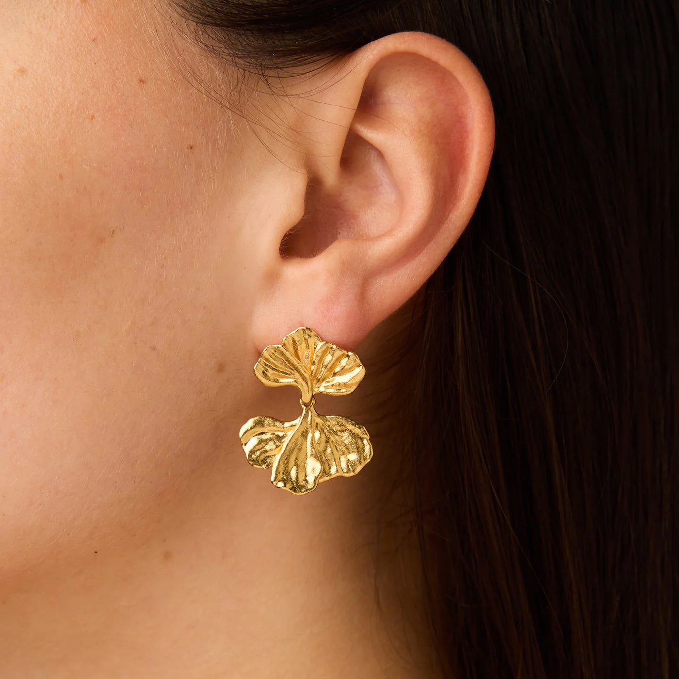 Gold leaf-shaped earrings worn by a person
