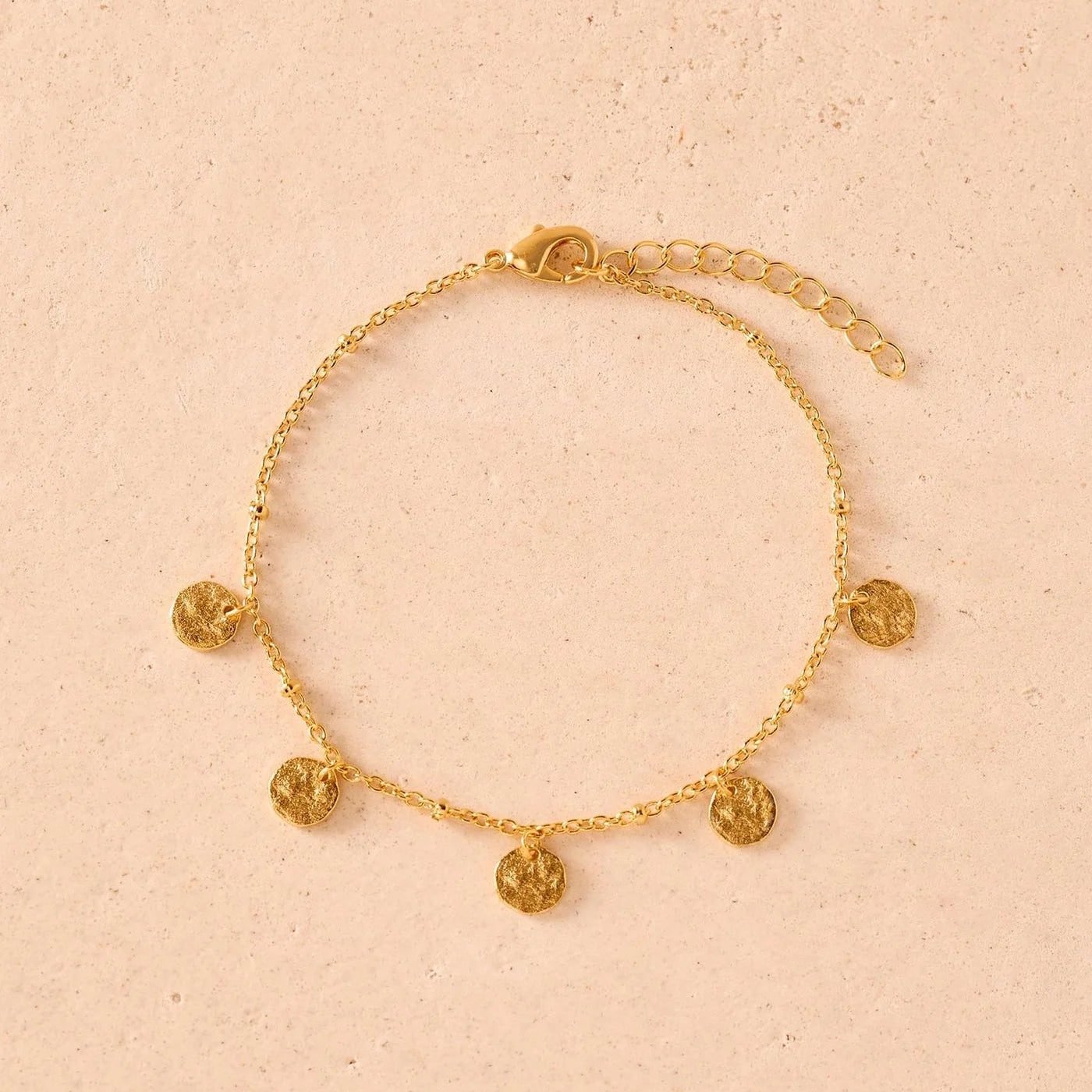 Gold bracelet with circular charms on a beige background