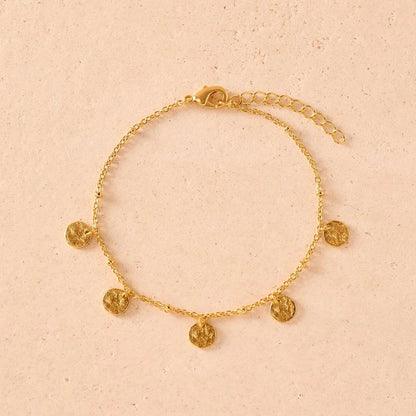 Gold bracelet with circular charms on a beige background