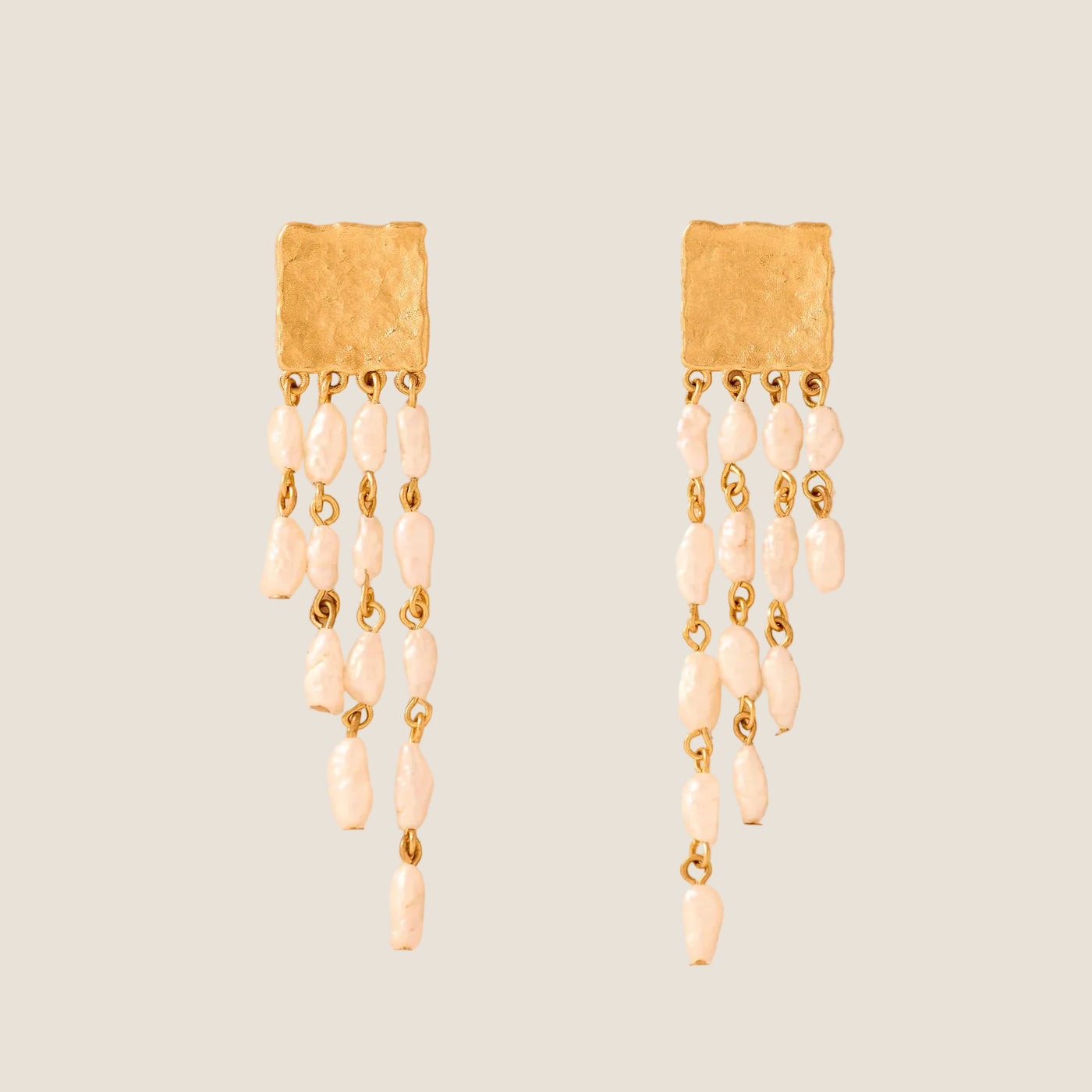 Pair of gold earrings with pearl-like beads on a beige background