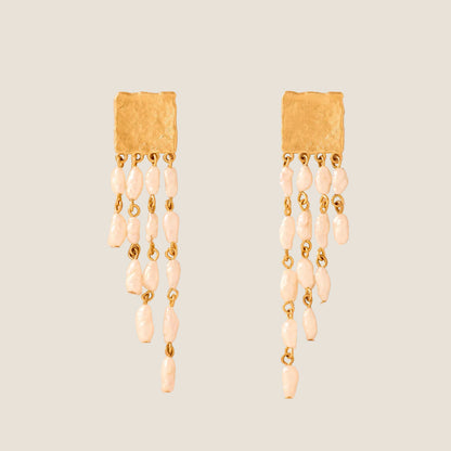 Pair of gold earrings with pearl-like beads on a beige background