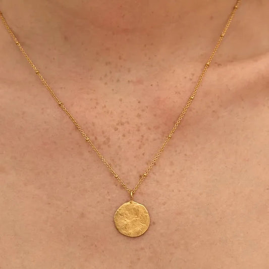 Gold necklace with a round pendant on a person's neck
