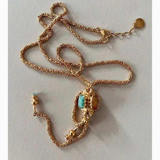 Long gold necklace with coloured talisman on neutral background