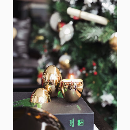 Elegant rose gold egg-shaped candle holders with a candle inside, alongside a xmas tree