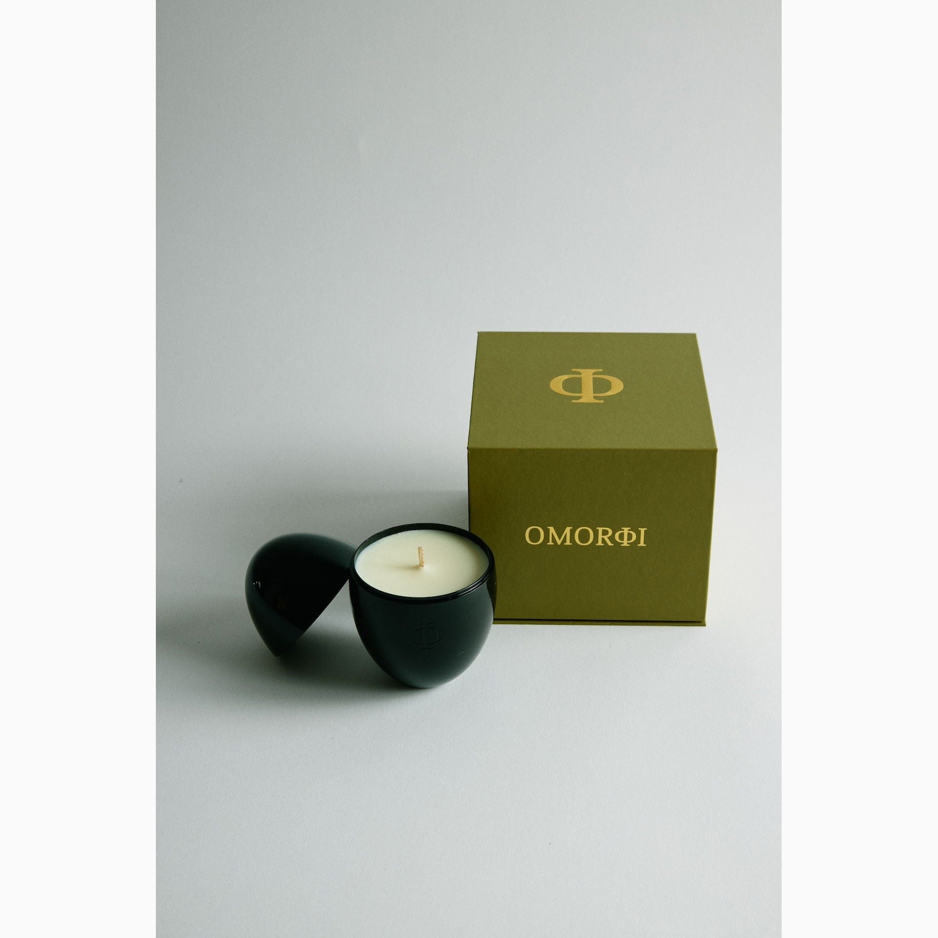 Elegant black egg-shaped candle holders with a candle inside, alongside a green box with omorfi logo 