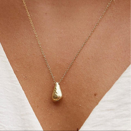 Gold necklace with a teardrop pendant on a person wearing a white top.
