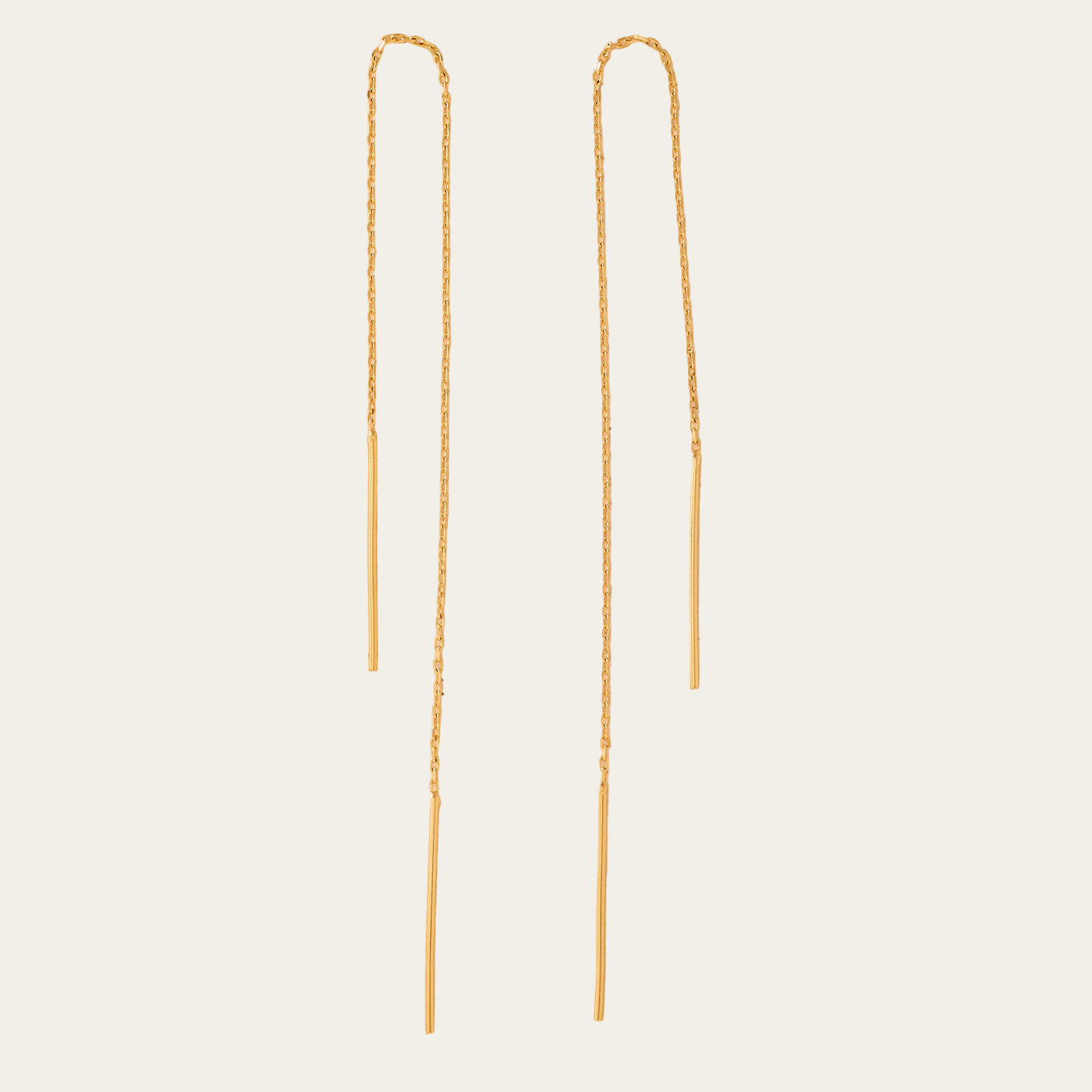 Two gold chain earrings on a beige background