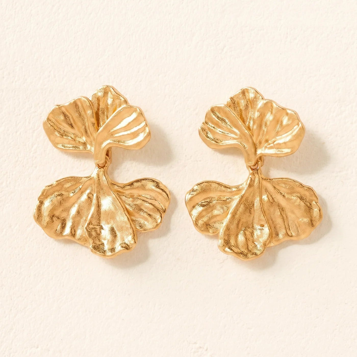 Pair of gold leaf-shaped earrings on a beige background