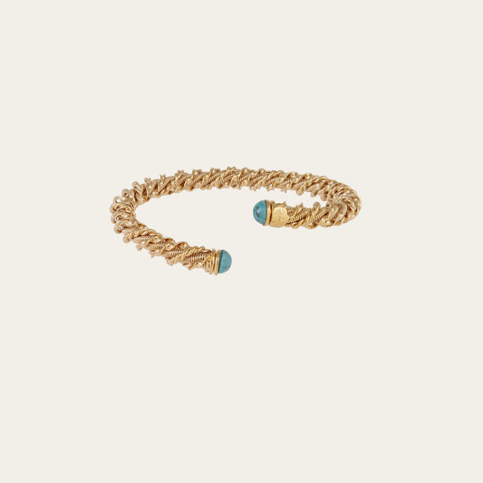 gold cuff bracelet with turquoise stones at the ends on neutral background