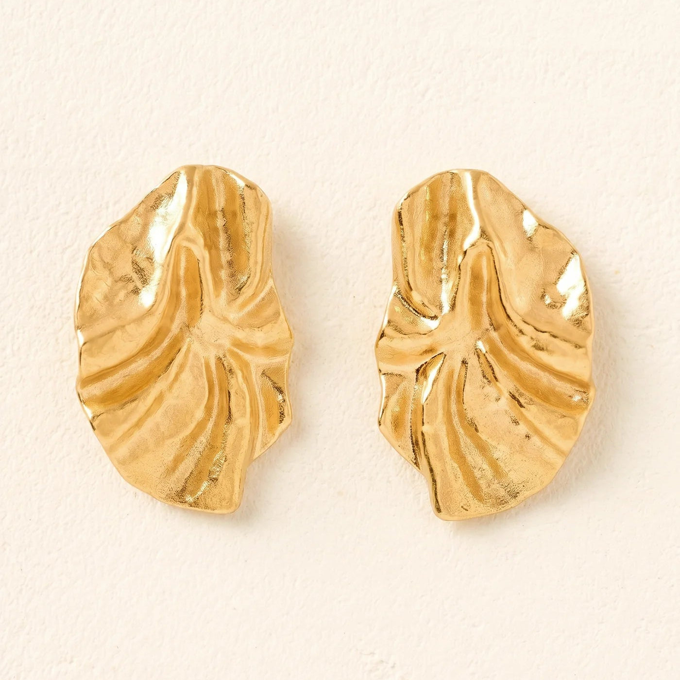 Gold leaf-shaped earrings on a beige background