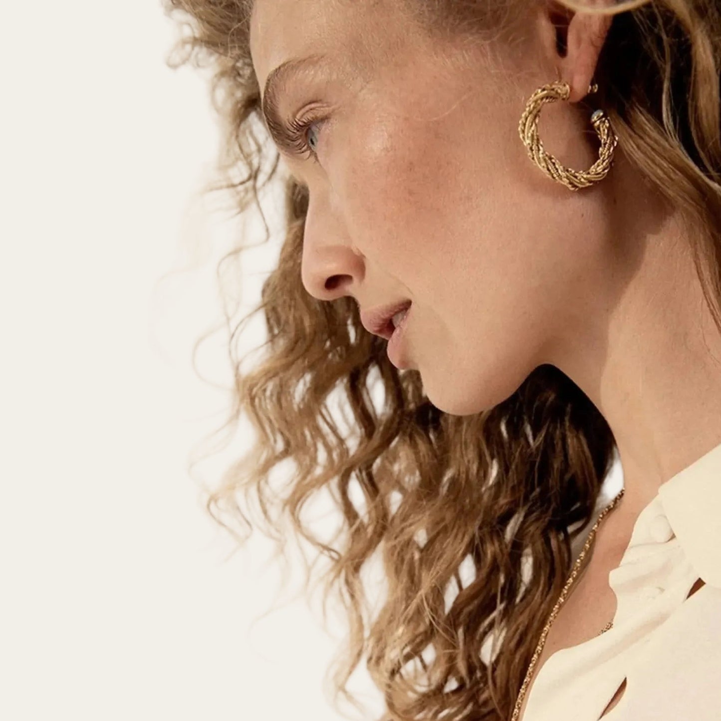 Gold braided hoop earrings worn by model in side profile view.”