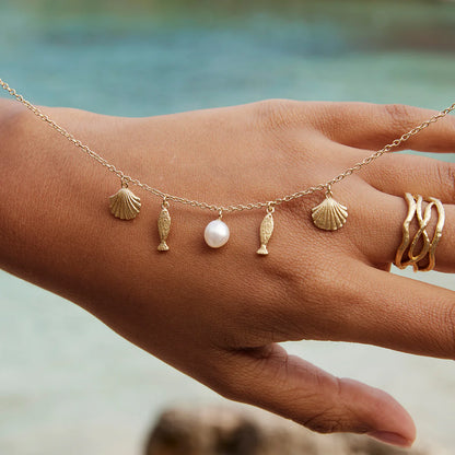 Hand with necklace with charms against a blurred natural background