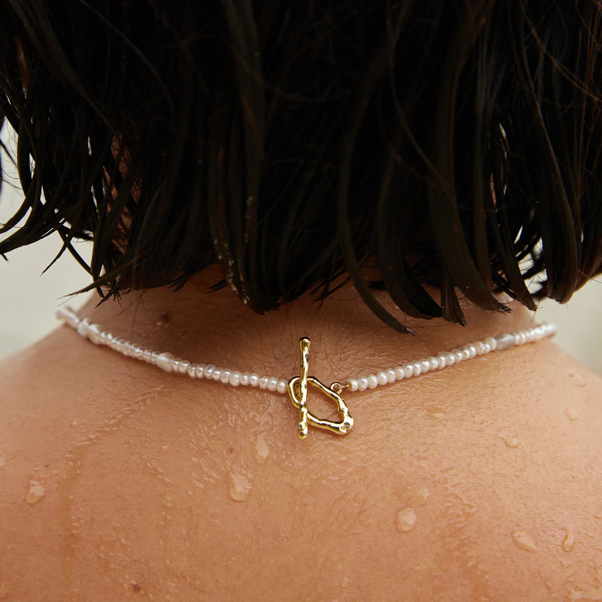 Pearl necklace with a gold pendant worn by a person with wet skin, possibly after a shower.