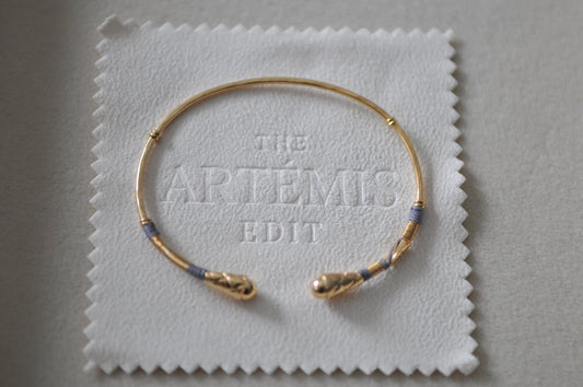 Gold bracelet on a white cloth with 'The Artemis Edit' branding.