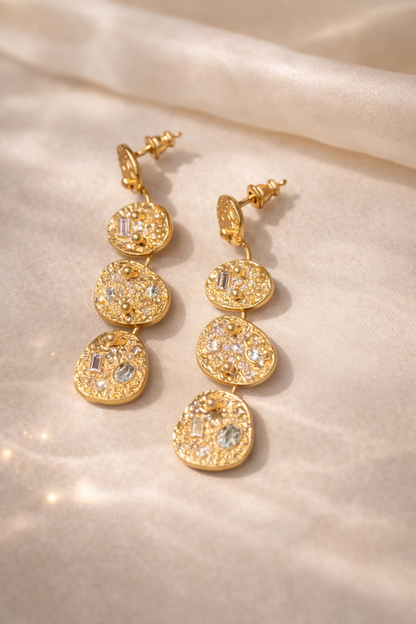 Gold earrings with circular designs on a beige fabric background