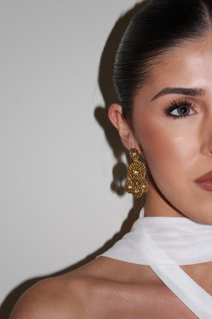 Woman wearing gold earrings with a neutral background