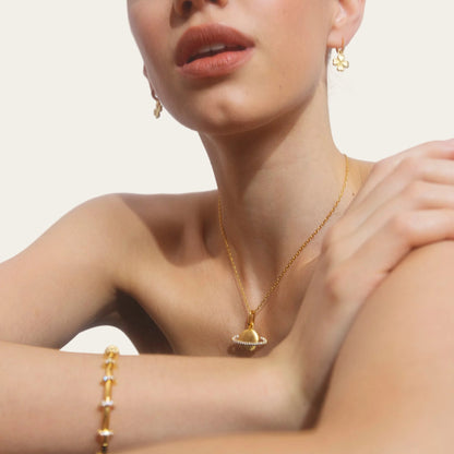 Woman wearing gold jewelry including earrings, necklace, and bracelet against a plain background