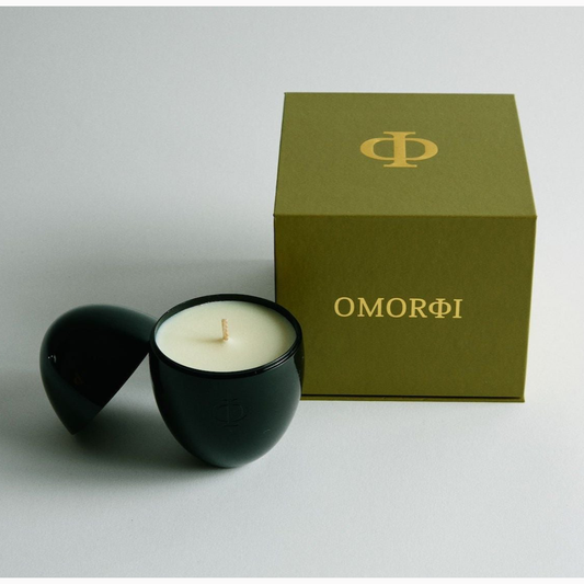 Black candle in a holder with a green box labeled 'OMORFI' on a light gray background