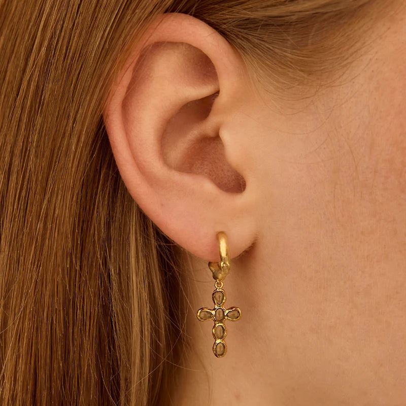 Gold cross earring worn by a person with brown hair.