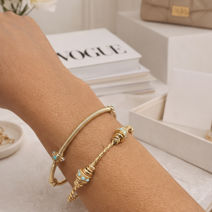 Gold bracelets on a wrist with a magazine and handbag in the background