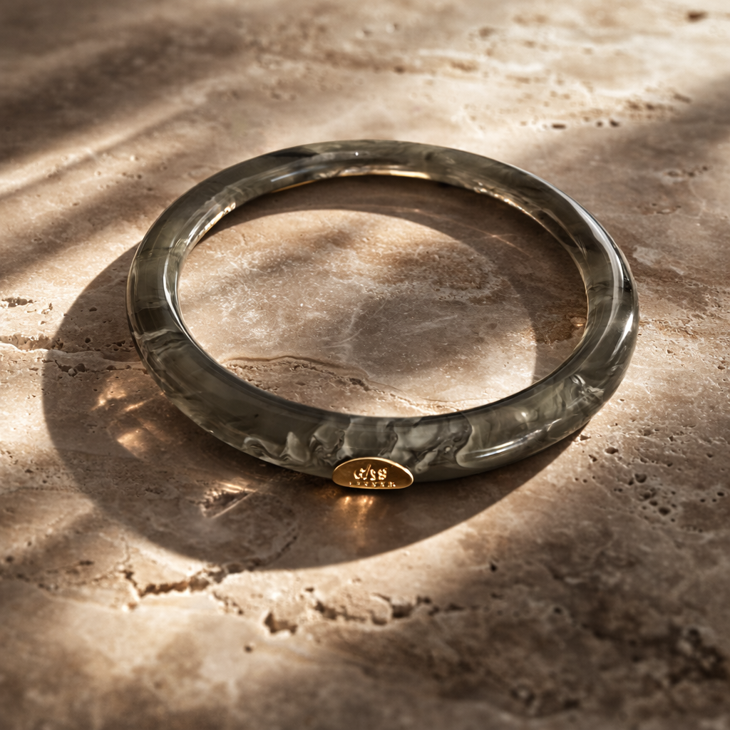 Green bangle with a gold tag on a textured stone surface