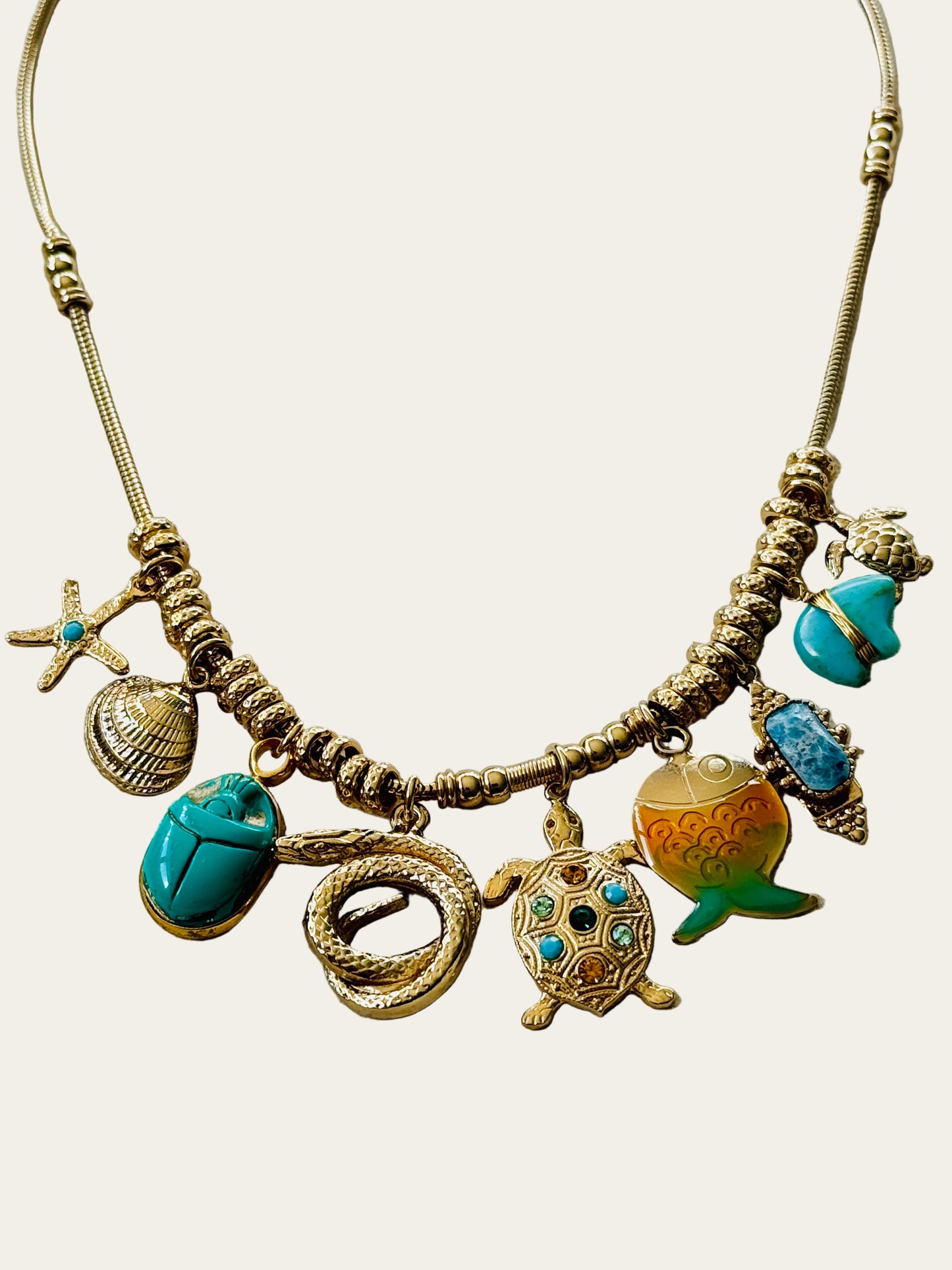 Necklace with various charms including a turtle, shell, and scarab on a neutral surface