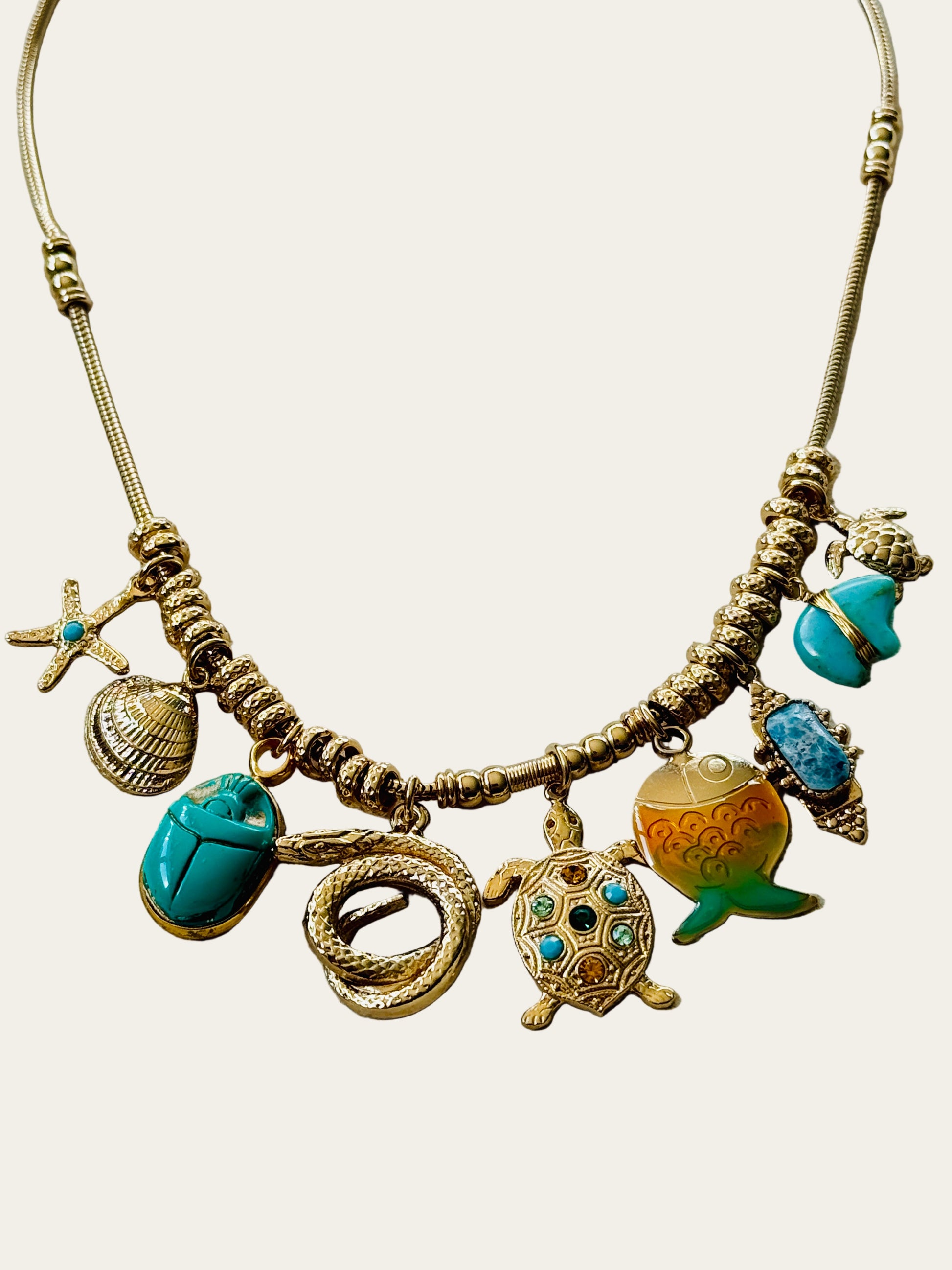 Necklace with various charms including a turtle, shell, and scarab on a neutral surface