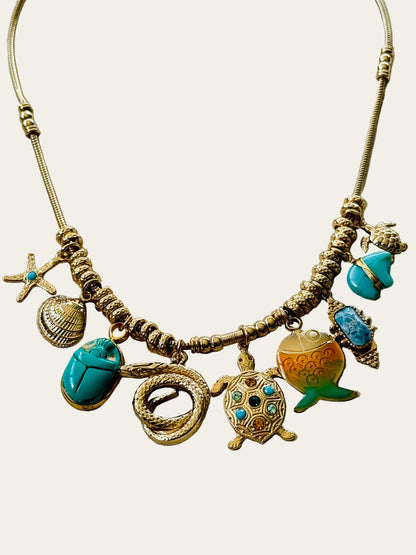 Necklace with various charms including a turtle, shell, and scarab on a neutral surface