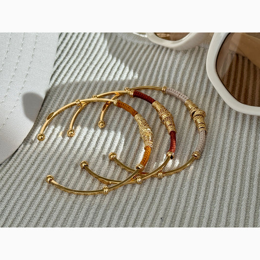 Set of gold bracelets with red accents on a textured surface