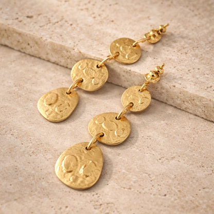 Gold earrings with circular pendants on a beige stone surface