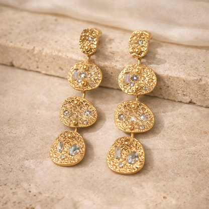 Gold earrings with gemstones on a beige stone surface