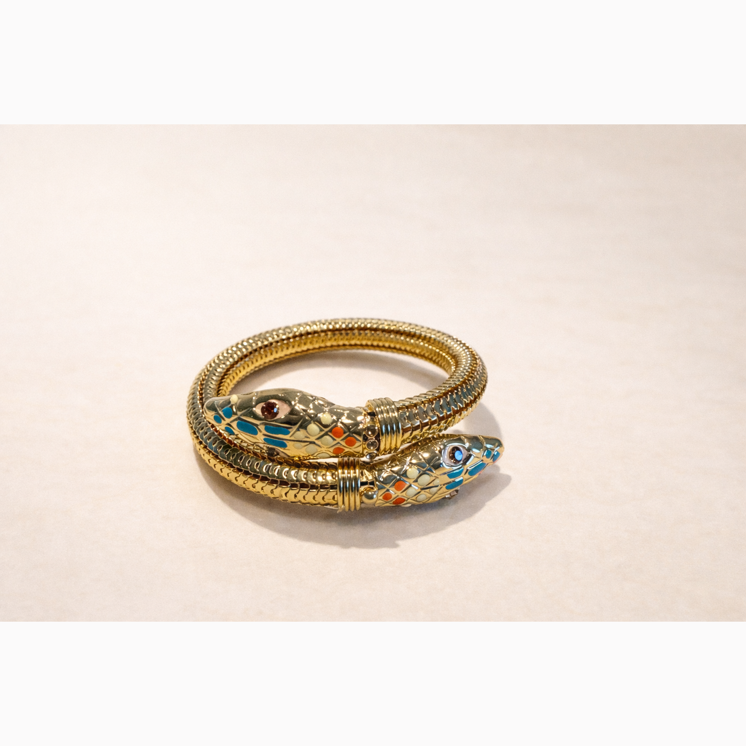 Gold snake-shaped bracelet with colorful accents on a beige background