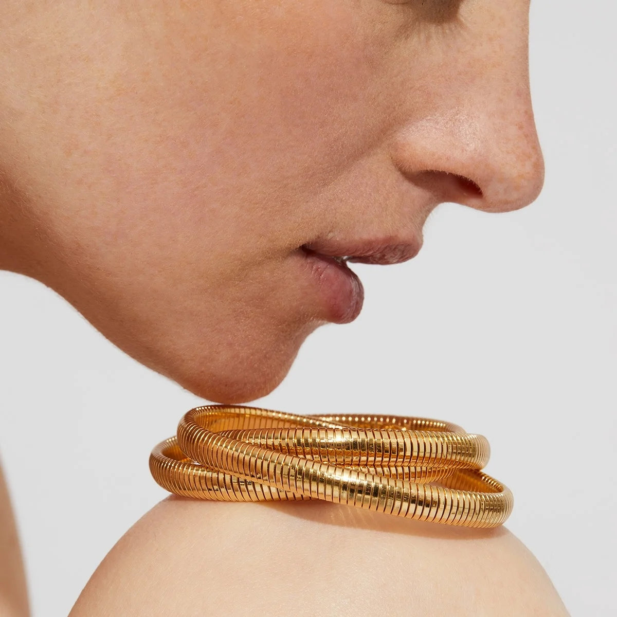 Close-up of a person wearing a gold bracelet on a neutral background