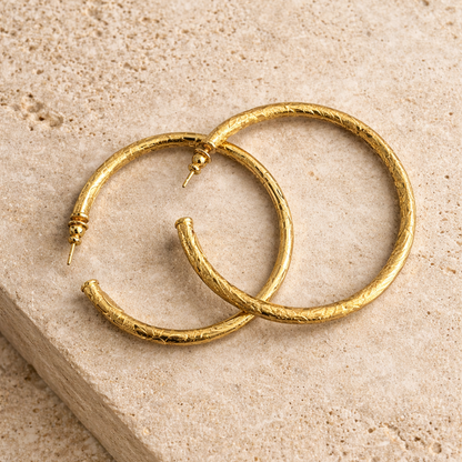 Gold hoop earrings on a beige stone surface